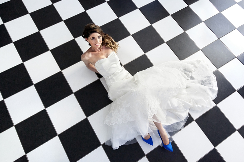 Bride wearing lace dress, with blue shoes, lying on a black and white checked floor at Estuary Hotel, Port Edward.