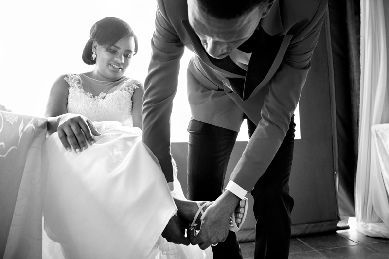 Black and white photograph, groom helping bride with broken shoe at Valverde Eco Hotel.