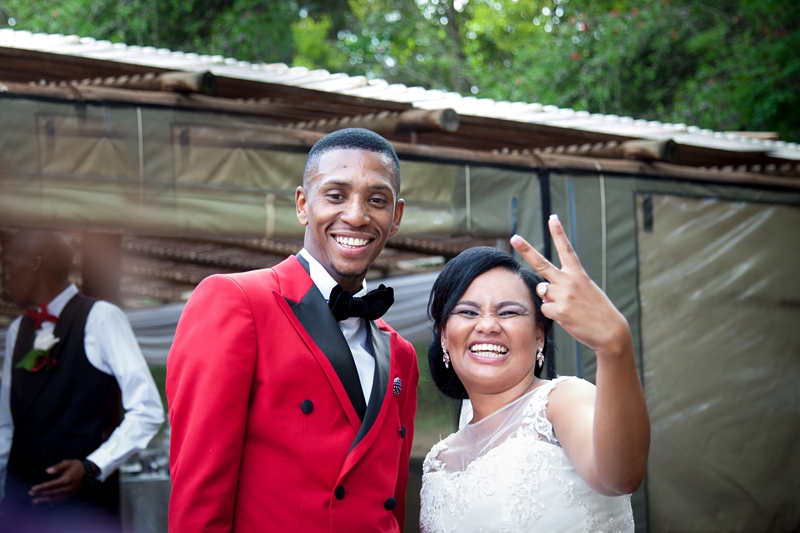Groom wearing red jacket laughing with bride showing peace sign at Valverde Eco Hotel.
