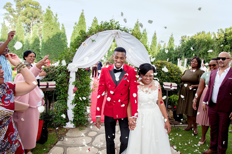 Bride and groom pulling funny faces while guests throw rose petal confetti, at Valverde Eco Hotel.