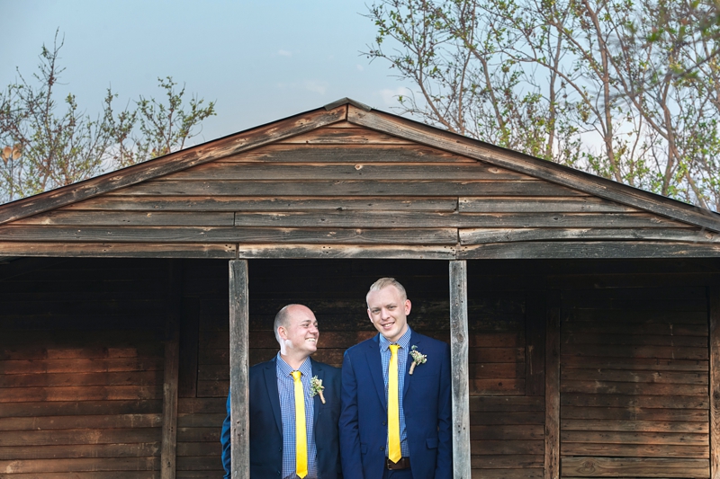 Grooms wearing blue suits with yellow ties, in front of wood cabin at Valverde Eco Hotel.
