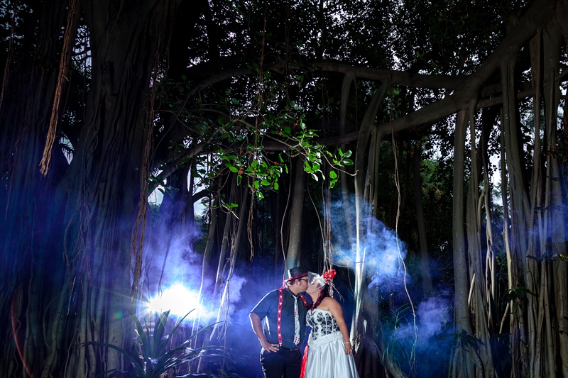 Alice in Wonderland themed bride and groom kissing under creepy trees,with purple smoke bombs, at Durban Botanical Gardens.