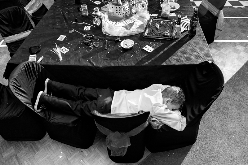 Child sleeping on chairs during Alice in Wonderland themed wedding reception.
