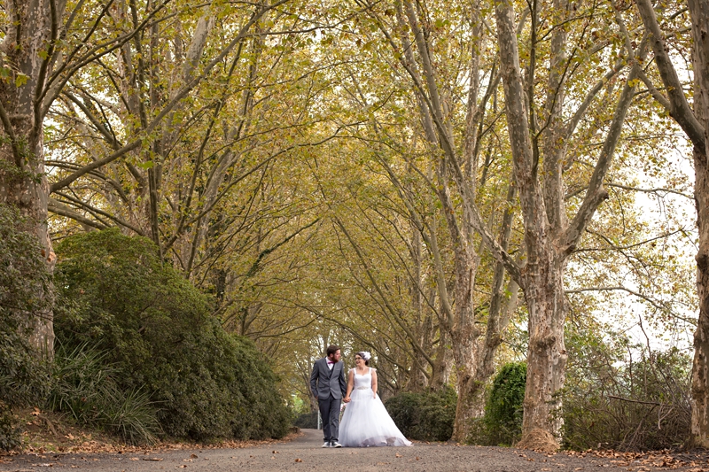 Bride and groom walking on tree lined road, at Shongweni Club.