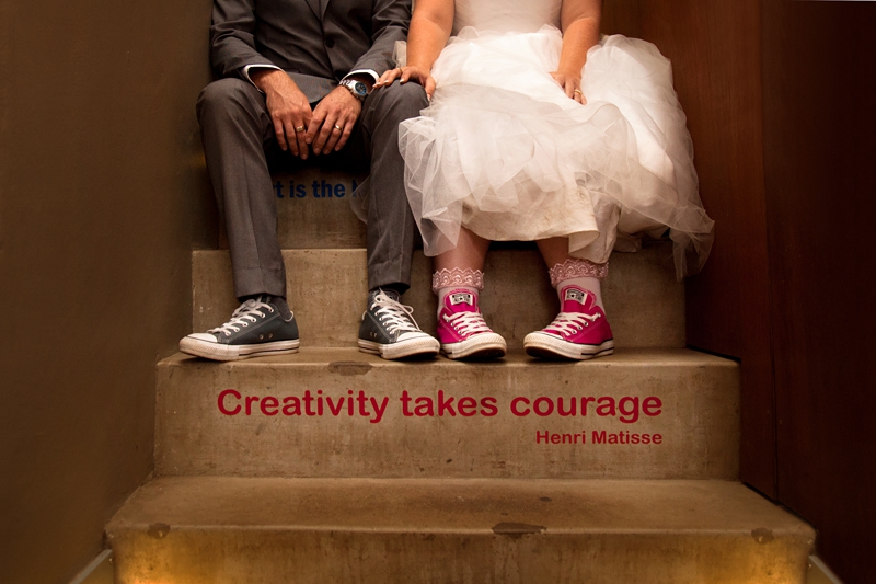 Bride and groom wearing converse shoes, sitting on steps with quote "Creativity takes courage," by Henri Matisse at Bellevue Cafe.