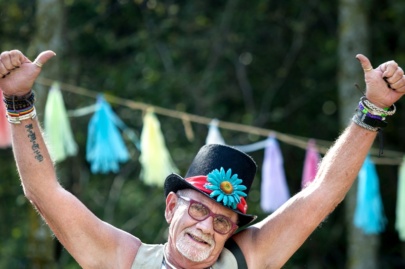 Man wearing a top hat with a blue flower, giving thumbs up, during Hippie Fest, at the Forest Venue.