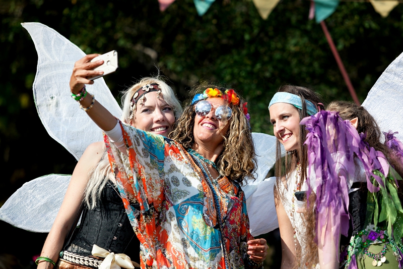 Hippie, with curly hair, taking a selfie with fairies during Hippie Fest, at the Forest Venue.