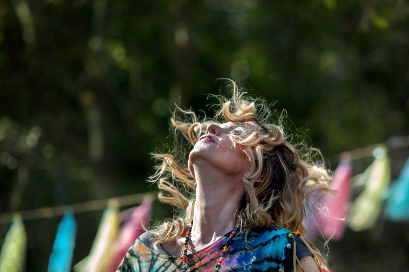 Hippie, with curly blonde hair and tie dye shirt, dancing in the sunlight during Hippie Fest, at the Forest Venue.