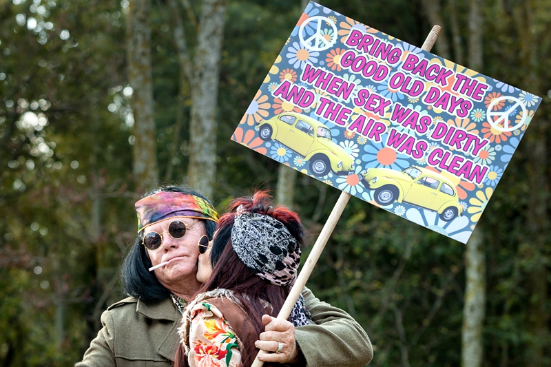 Hippies kissing while holding a sign reading,"Bring back the good old days when sex was dirty and the air was clean," during Hippie Fest, at the Forest Venue.