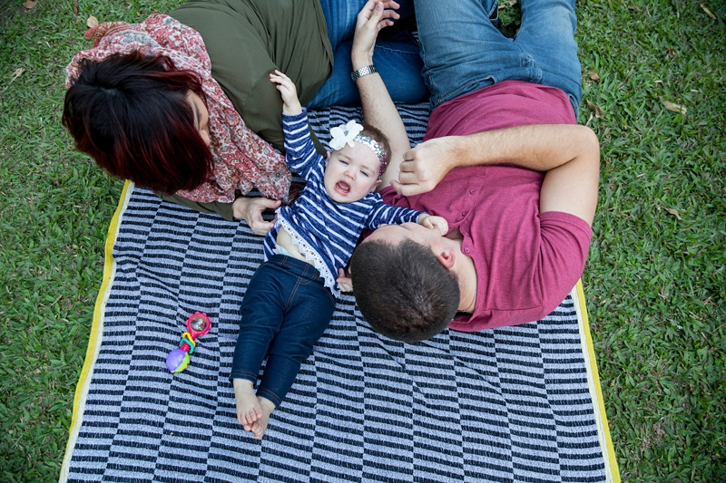 Parents lying on striped blanket with toddler, wearing a flower sequin headband, throwing a tantrum at Japanese Gardens, Pinetown.