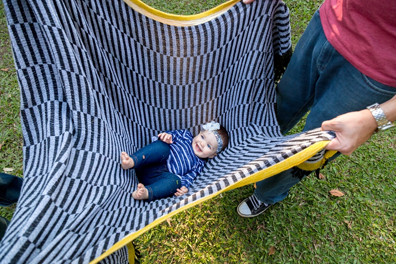 Parents swinging laughing girl toddler in striped blanket at Japanese Gardens, Pinetown.