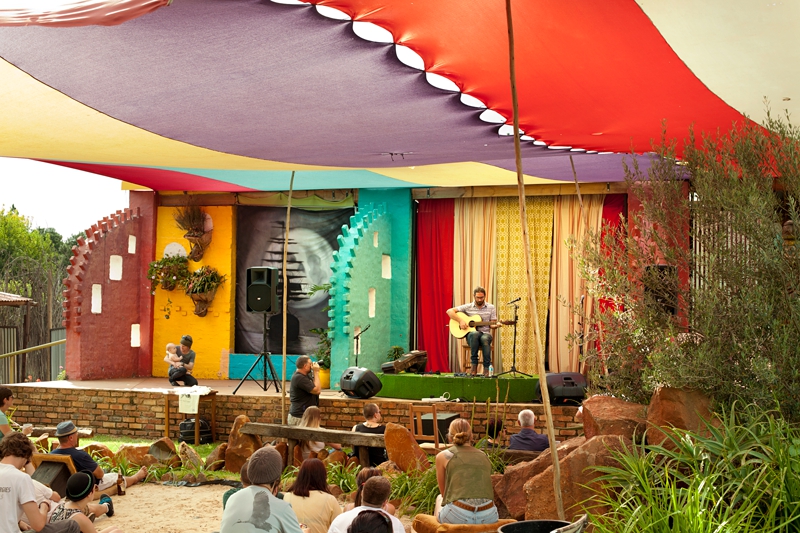 Guy Buttery, South African musician, playing his guitar, under colorful tent at Klitsgras Drumming valentines picnic.