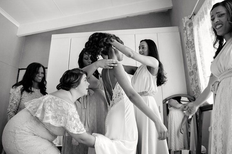 Bridesmaids helping bride into her wedding dress.