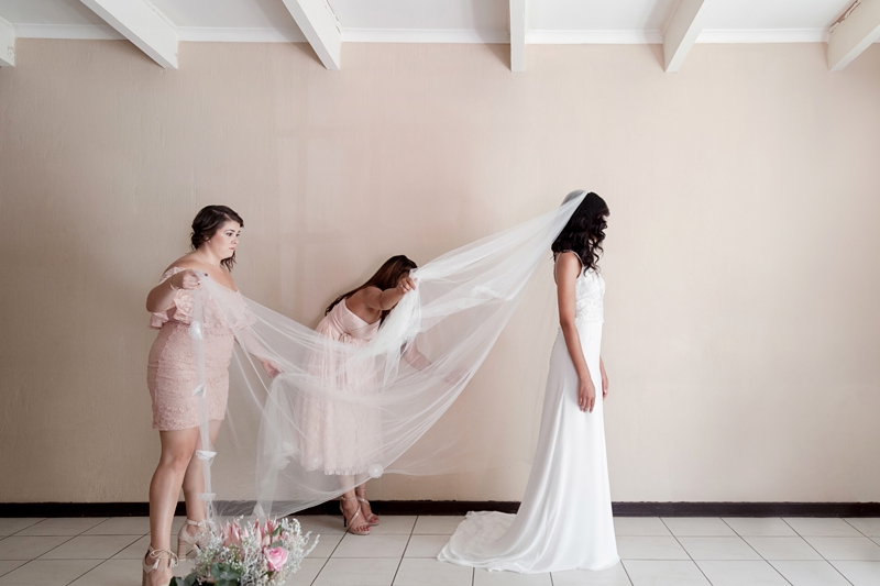 Bridesmaids, wearing peach dresses, straightening out brides long white veil.