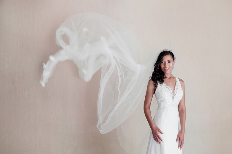 Bride wearing white, lace dress with long veil waving behind her.