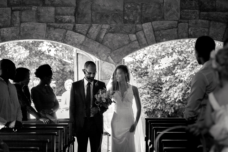 Bride smiling at her father, as they walk down the isle, at Leafy Green Cafe.