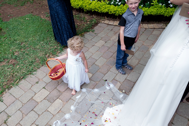 Flower girl throwing red rose petals onto brides long veil at Leafy Green Cafe.