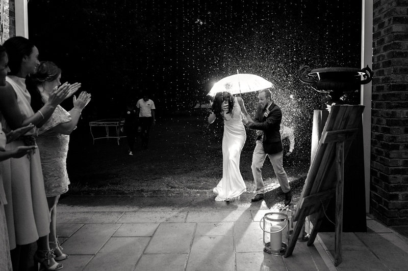Bride and groom running in the rain, with an umbrella to the reception hall at Leafy Green Cafe.