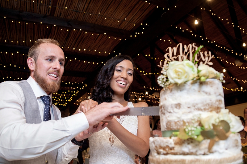 Bride and groom laughing, while cutting wedding cake, at Leafy Green Cafe.