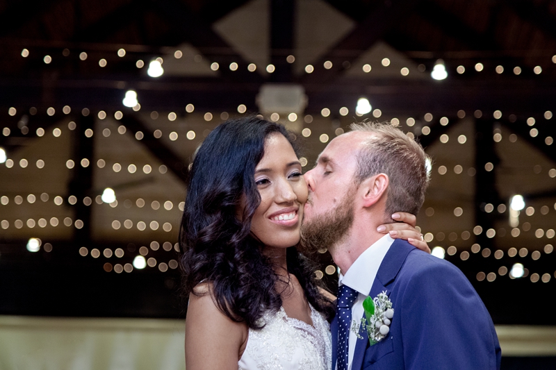 Groom kissing bride on the cheek, during reception, at Leafy Green Cafe.