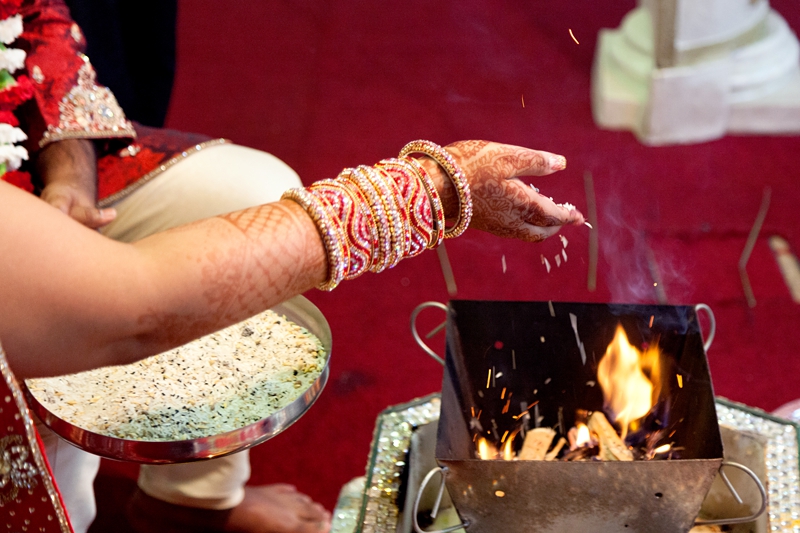 Bride throwing rice into fire during Hindu wedding ceremony at Shree RadheShyam Mandir.