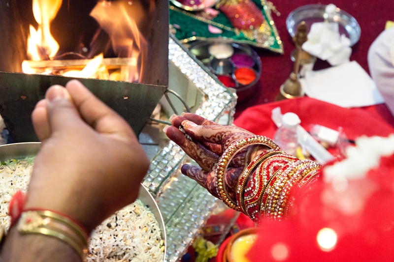 Bride and groom throwing rice into fire during Hindu ceremony at Shree Radhe Shyam Mandir.
