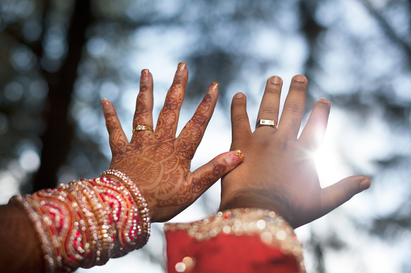 Brides hand with wedding mhendi next to grooms hand,wearing wedding rings, at Field and Study Centre.