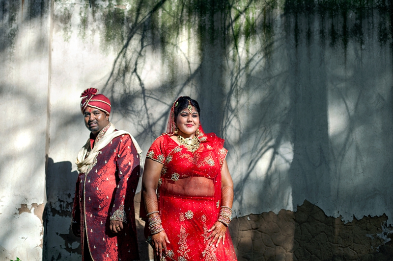 Bride and groom wearing traditional Hindu wedding outfit, with tree shadows behind them at Field and Study Centre.