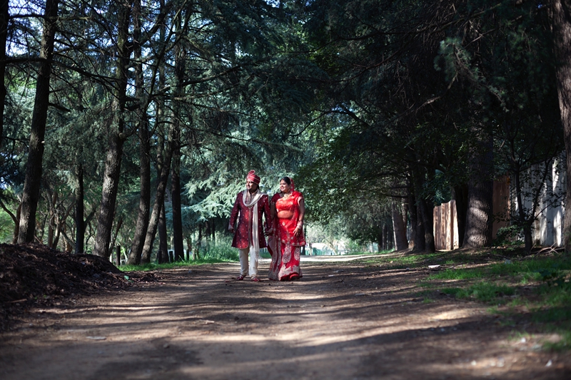 Bride and groom wearing traditional Hindu wedding outfit, walking down a forest road at Field and Study Centre.