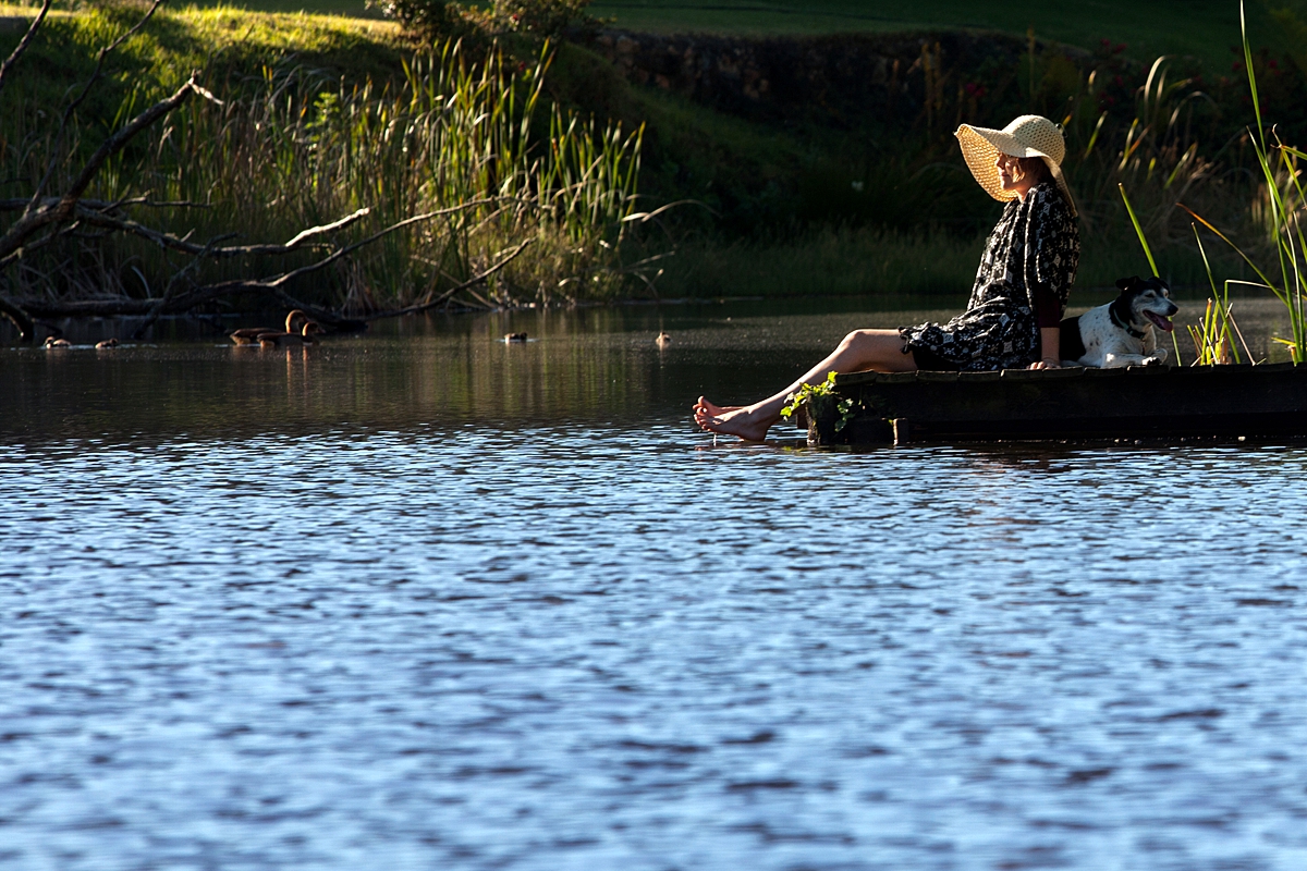 Lady wearing a hat sitting on a jetty with her feet in the water.